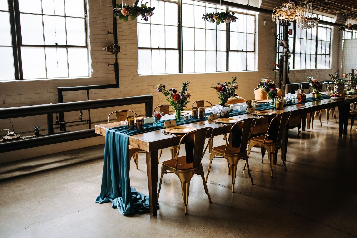 Long reception table set with blue runners and industrial chairs in a modern warehouse venue.