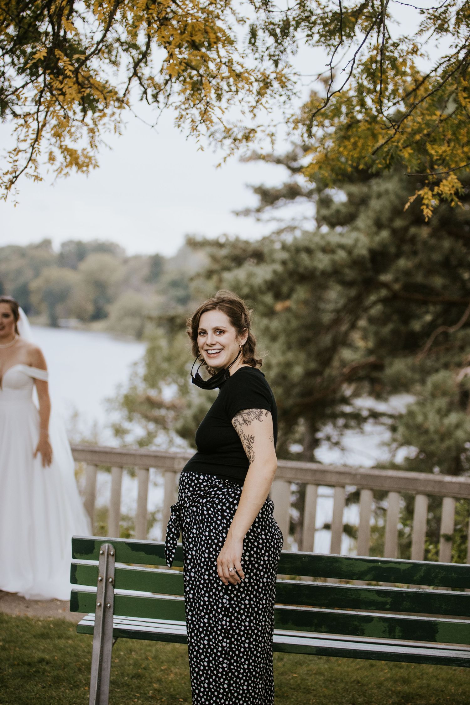 Person in polka dot dress standing on wooden deck overlooking water.