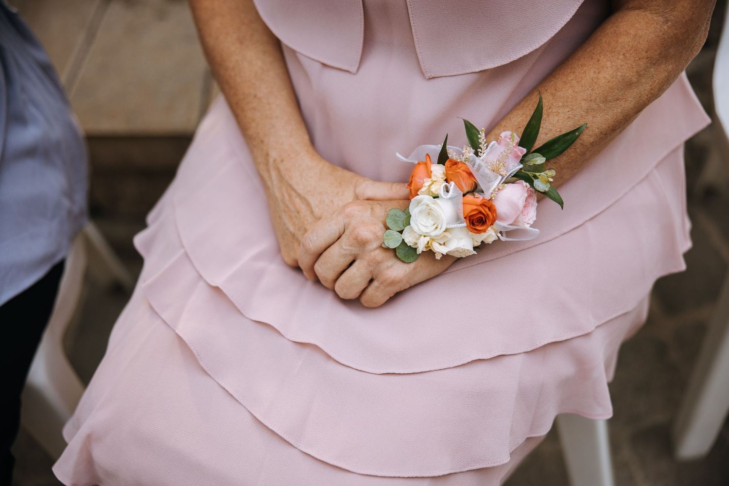 A person wearing a pink layered dress holds a delicate floral corsage with white and coral flowers.