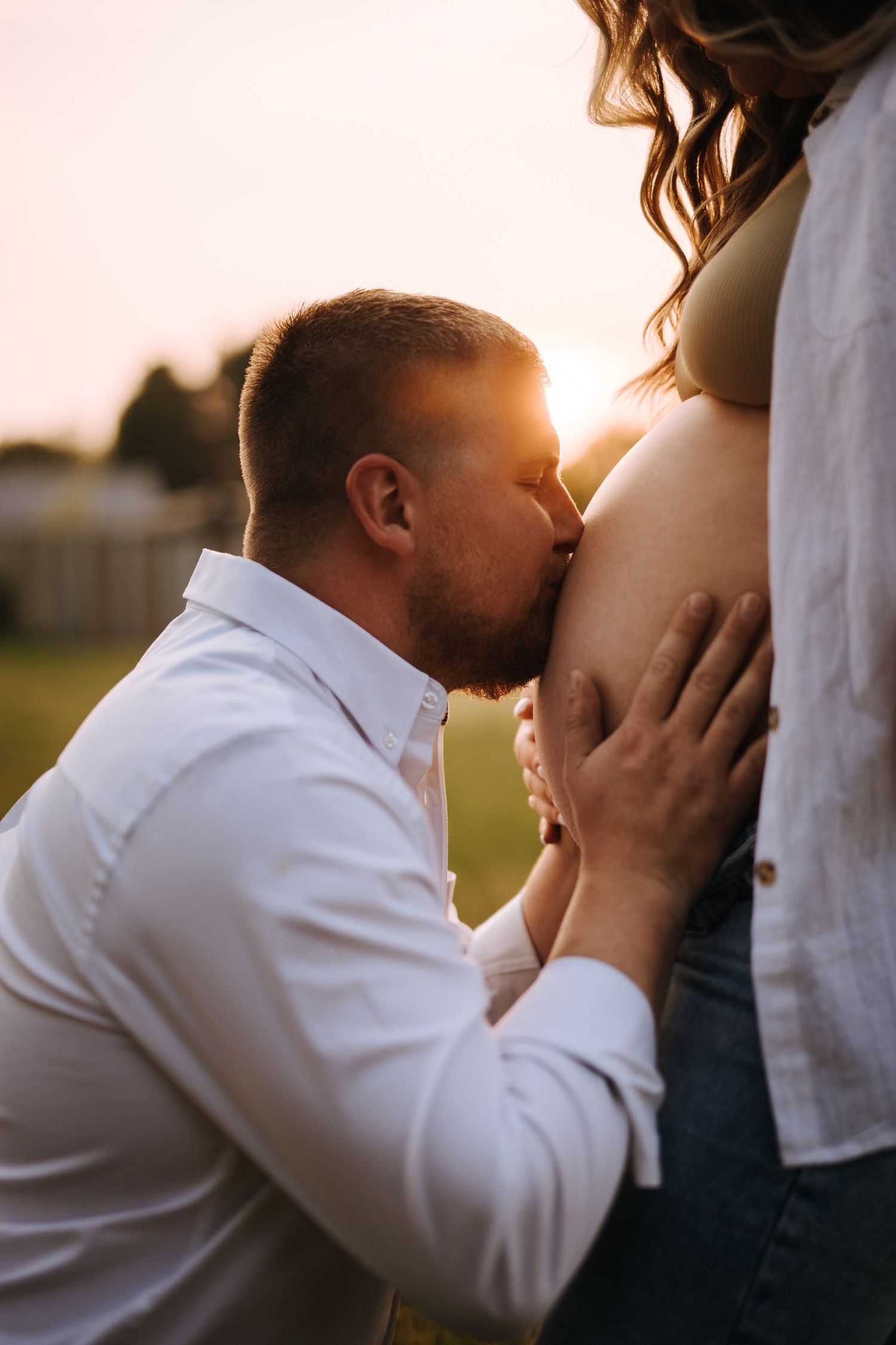 Intimate maternity portrait captured in warm sunset lighting outdoors.