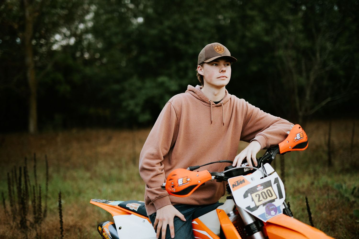Action shot of someone riding an orange dirt bike through wooded terrain.