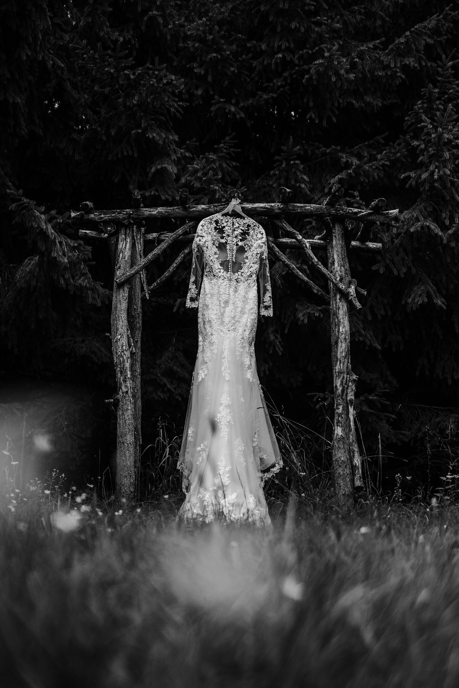 Black and white photo of a wedding dress hanging between trees in a dreamy outdoor setting.