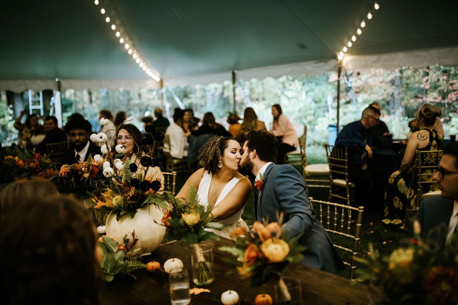 Wedding reception guests seated at round tables with string lights overhead creating a warm, celebratory atmosphere.