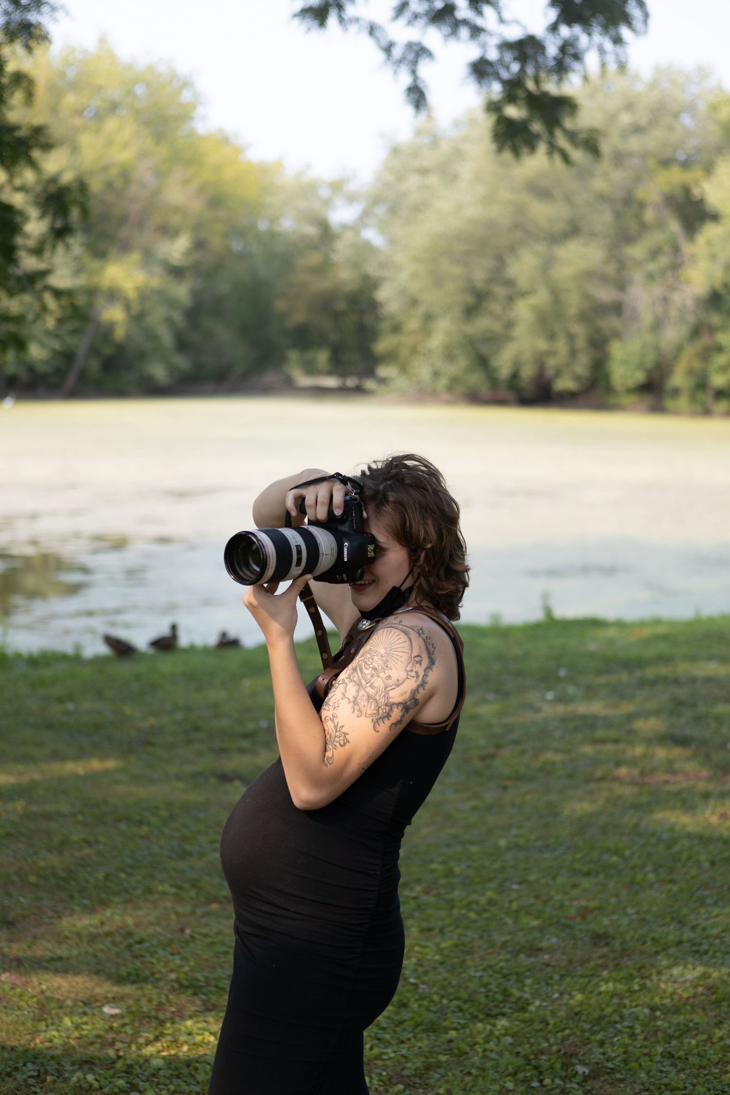 Photographer with tattoos using professional camera equipment outdoors.