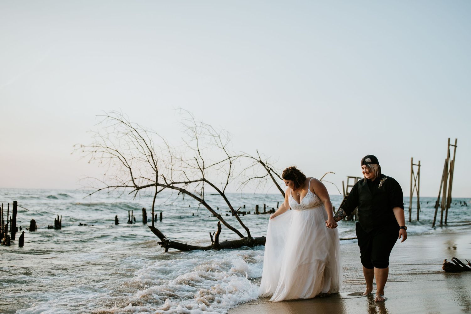 A couple walks along a moody beach with driftwood and waves during an overcast day at Hunting Island, South Carolina.