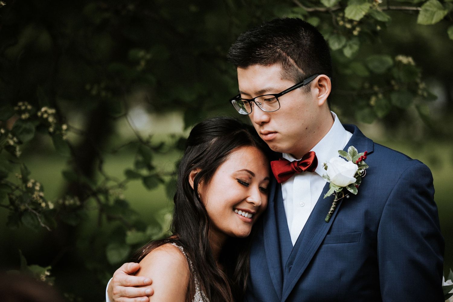 A couple in formal wedding attire shares an intimate moment together in a lush outdoor garden setting.