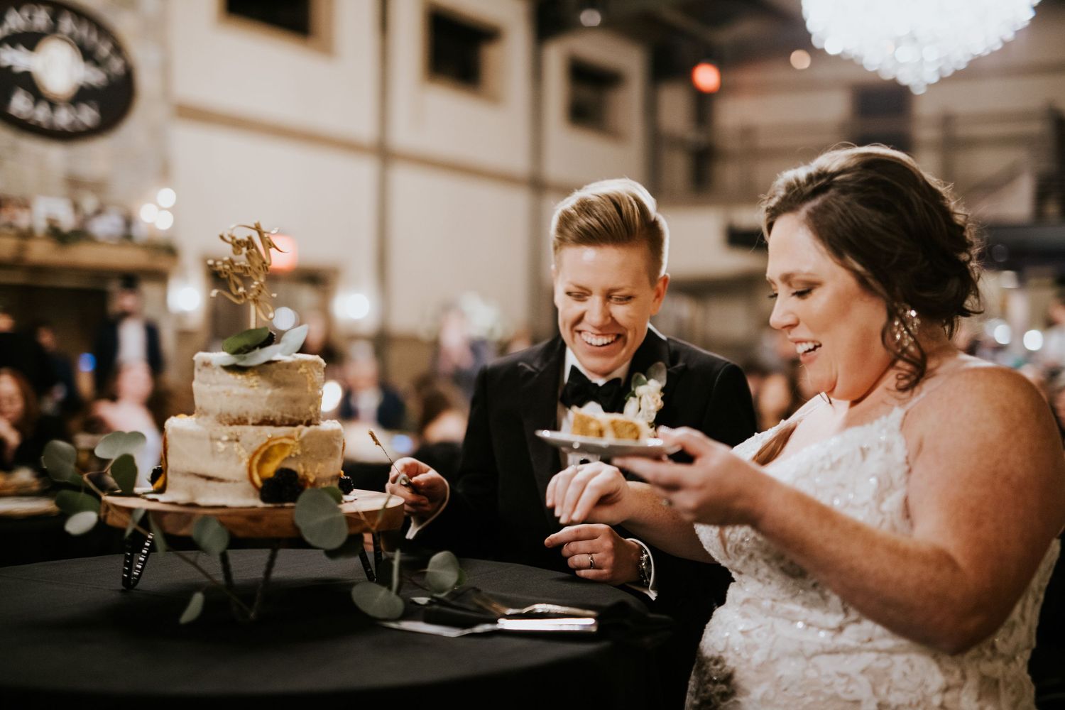 A joyful couple shares a laugh while cutting their rustic wedding cake at their reception celebration.