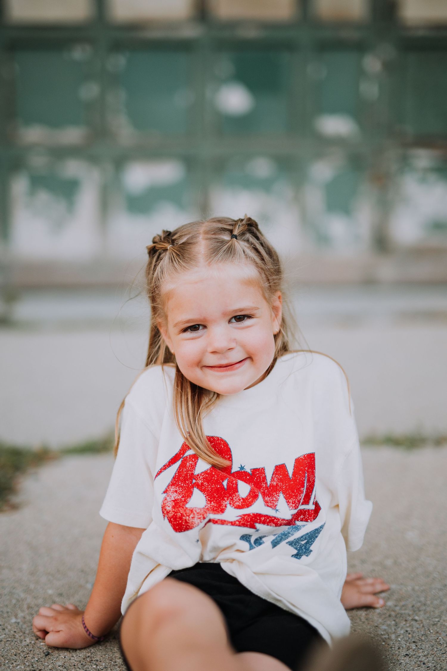 A young child in a white t-shirt with red design lays playfully on a concrete surface.