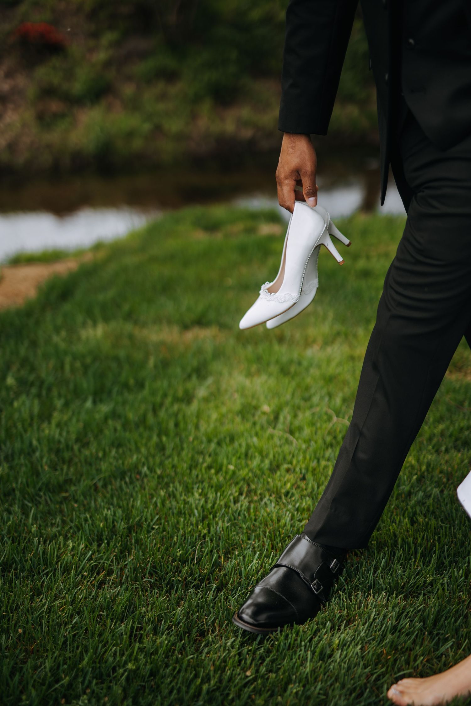 Close-up of formal shoes and white heels on green grass during wedding photoshoot.