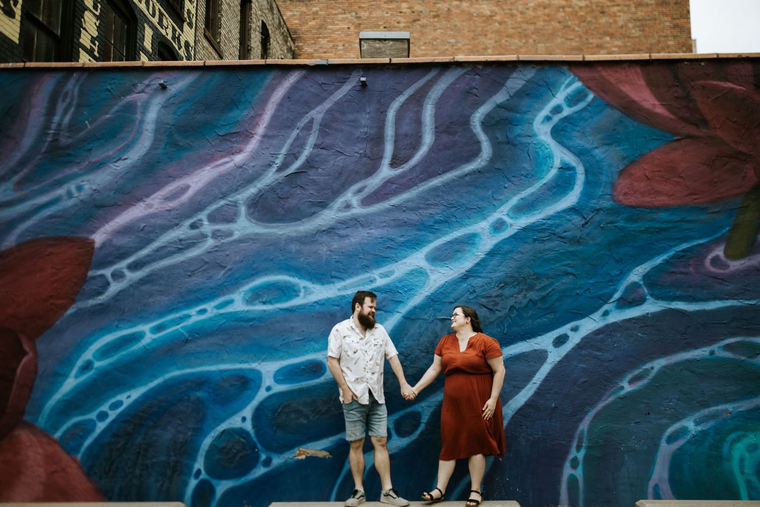 Couple poses in front of large blue and white abstract mural artwork.