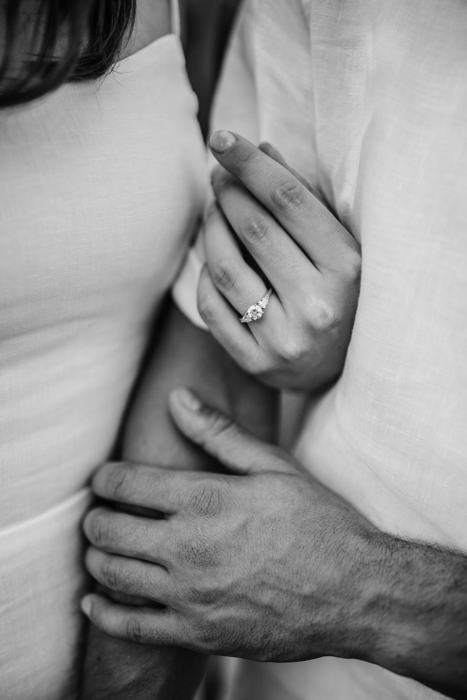 Close-up black and white photo of hands with an engagement ring showing tender affection.