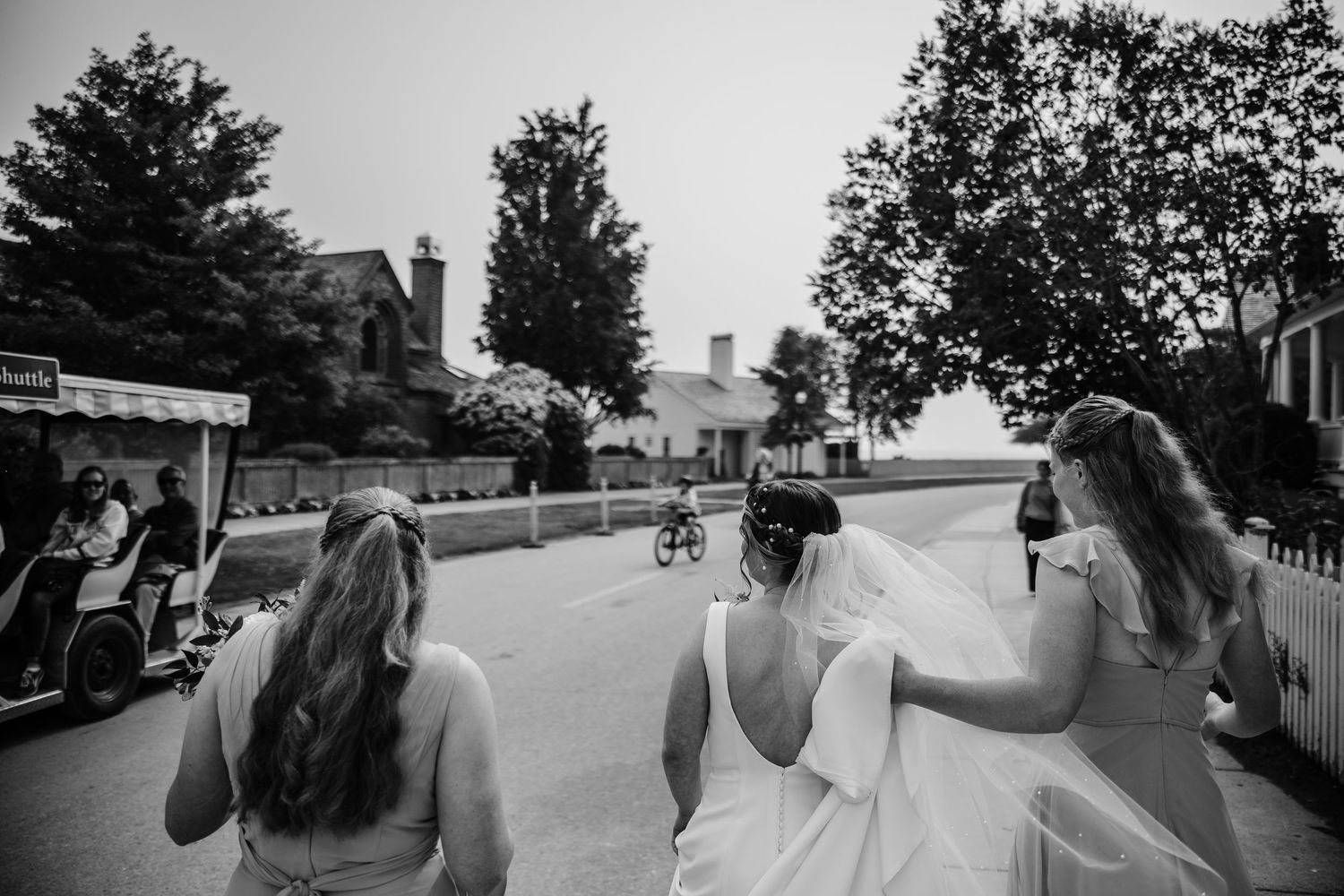 Black and white panoramic shot of wedding party walking down a tree-lined street.