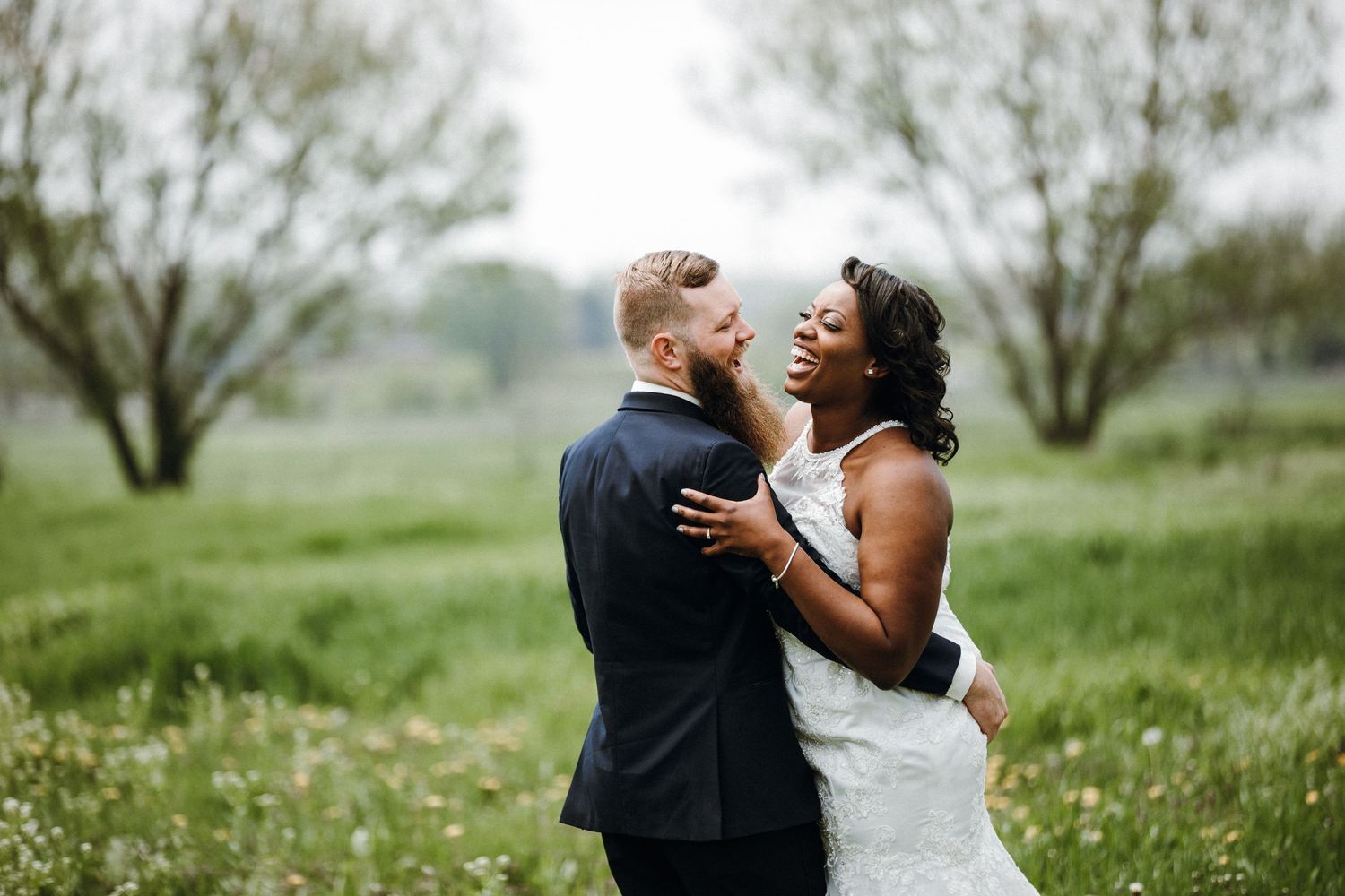 A romantic couple embraces in a lush green meadow filled with wildflowers on their wedding day.