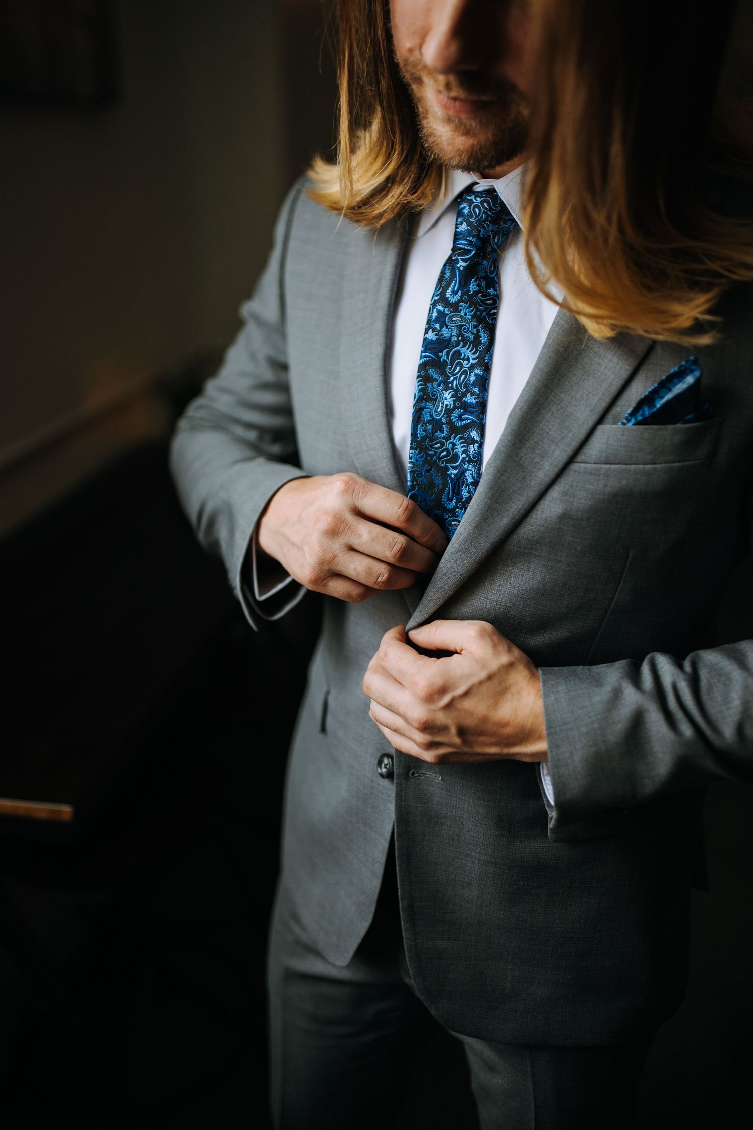 Close-up of grey suit jacket with sparkly blue tie in dramatic lighting.