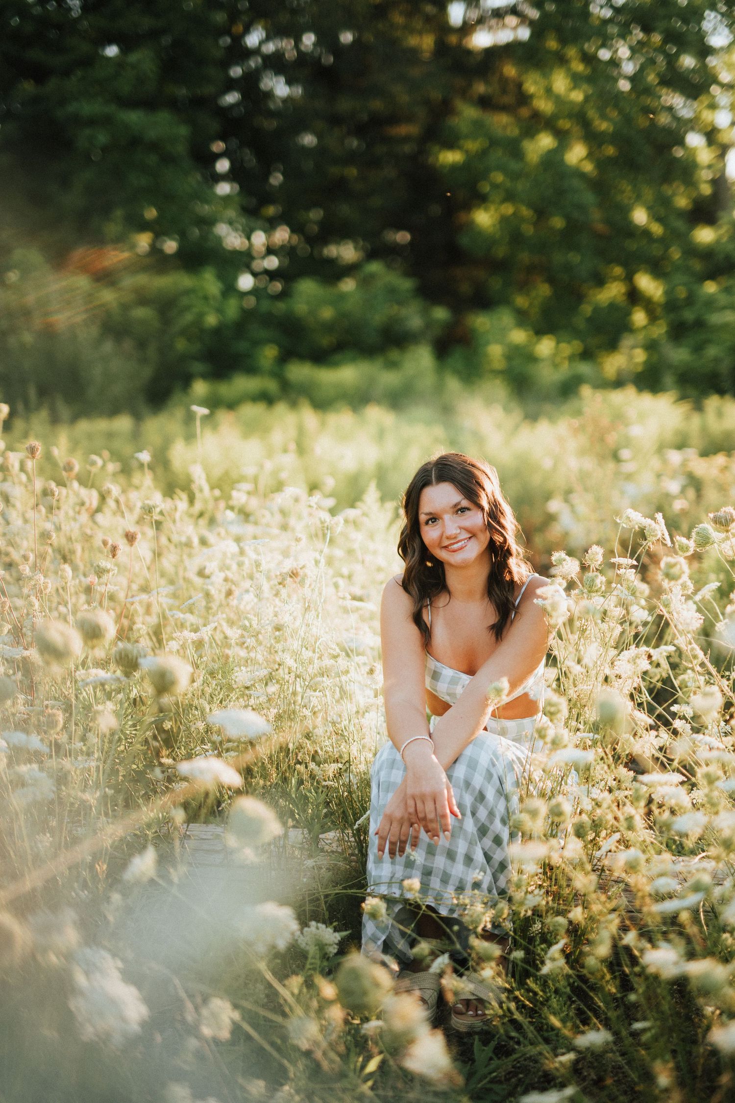 A white sundress stands out against wildflowers and tall grass in a golden summer field at sunset.