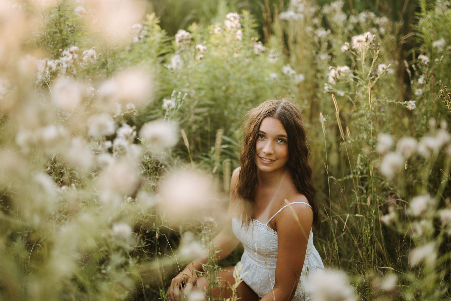 Person posing in a field of white wildflowers during golden hour.