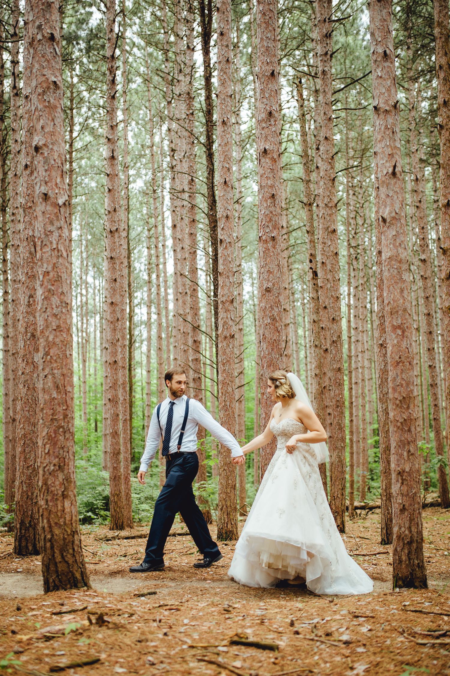 Playful wedding poses captured in a pine forest setting.