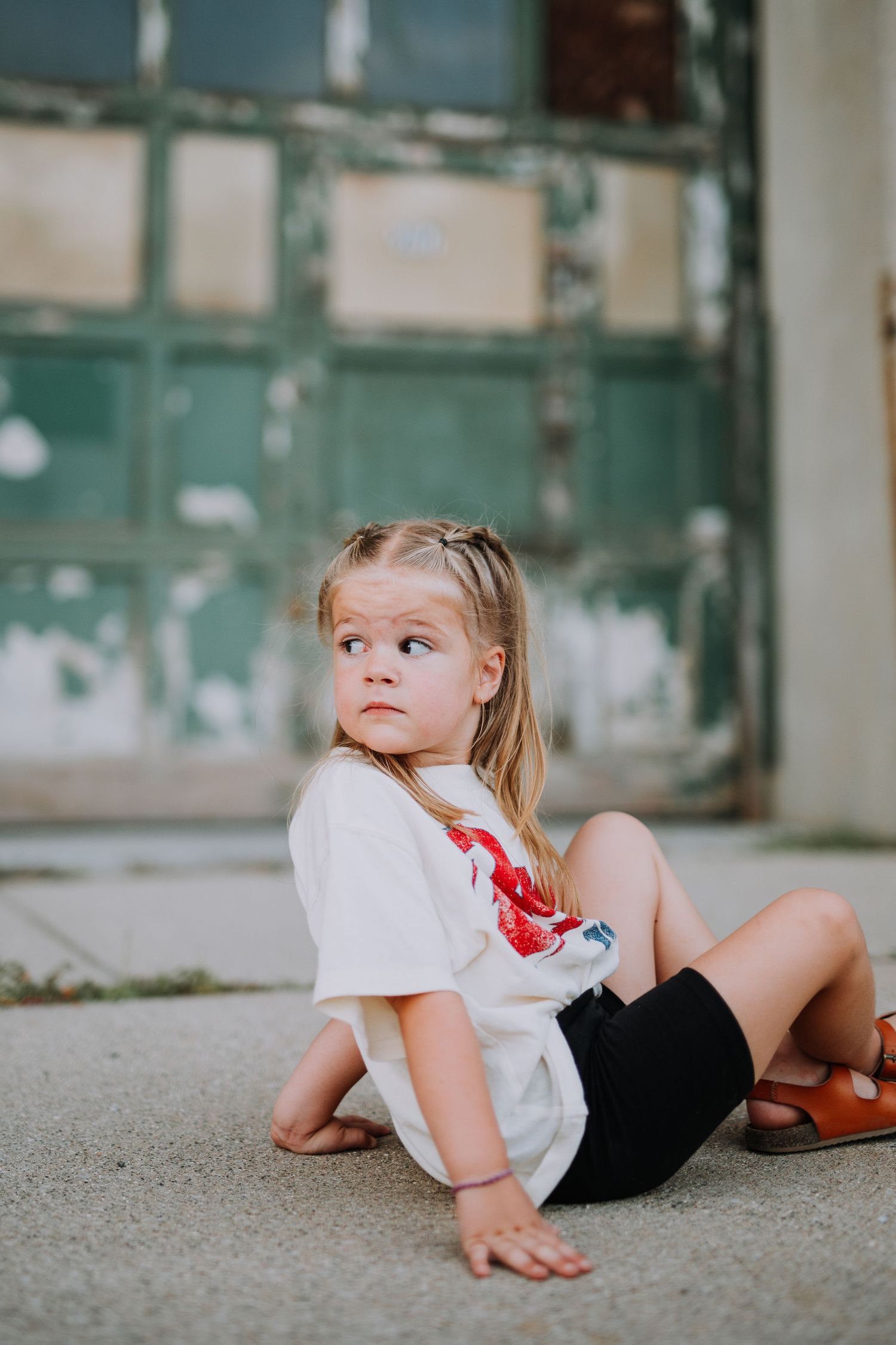 Child lying on ground wearing casual attire against green background.
