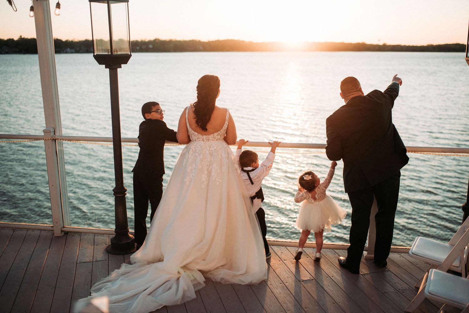 A wedding party watches the sunset from a waterfront deck.