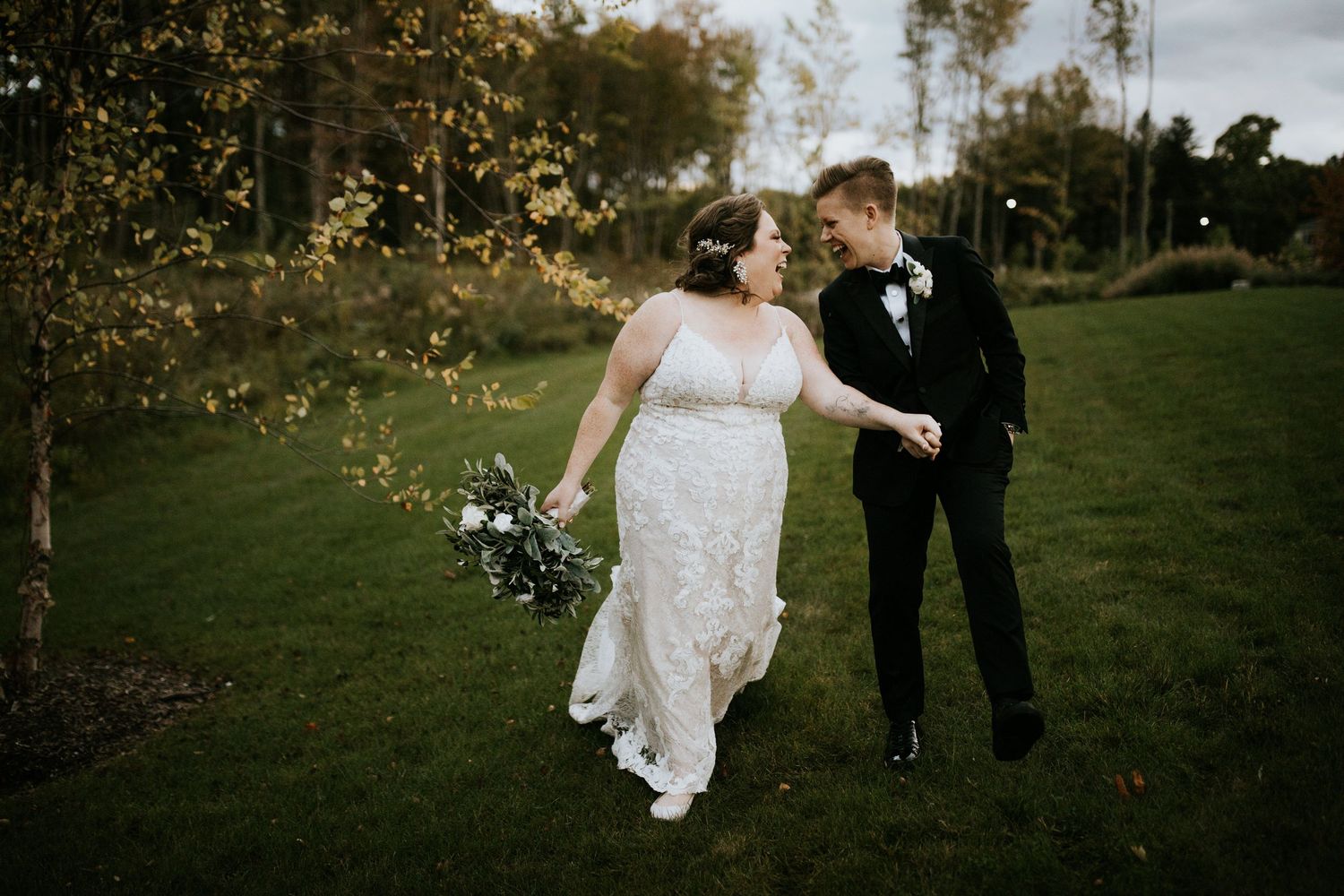 A couple in wedding attire strolls through an autumn garden setting with golden sunlight filtering through trees.