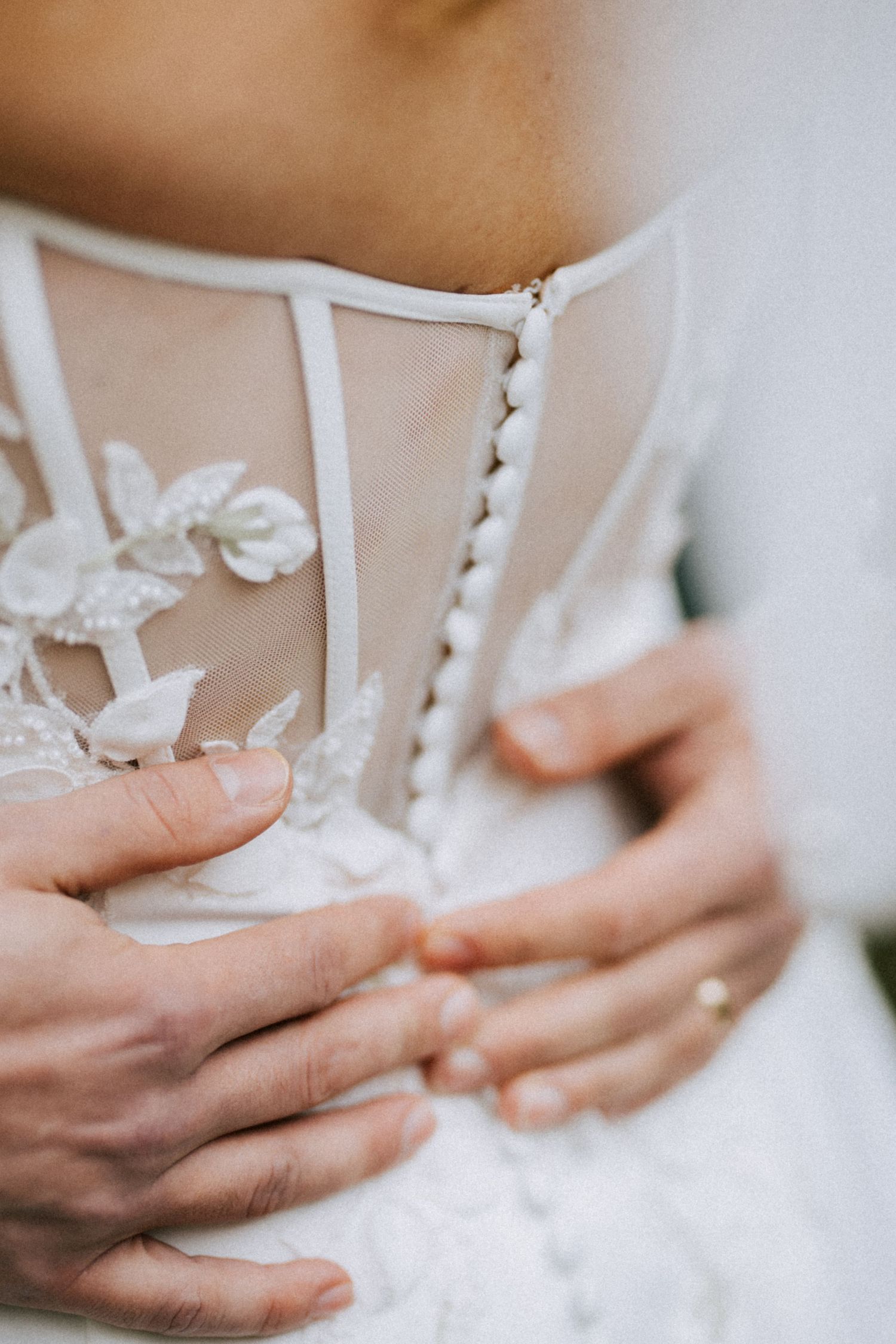 Close-up detail of delicate white lace and buttons on wedding dress.