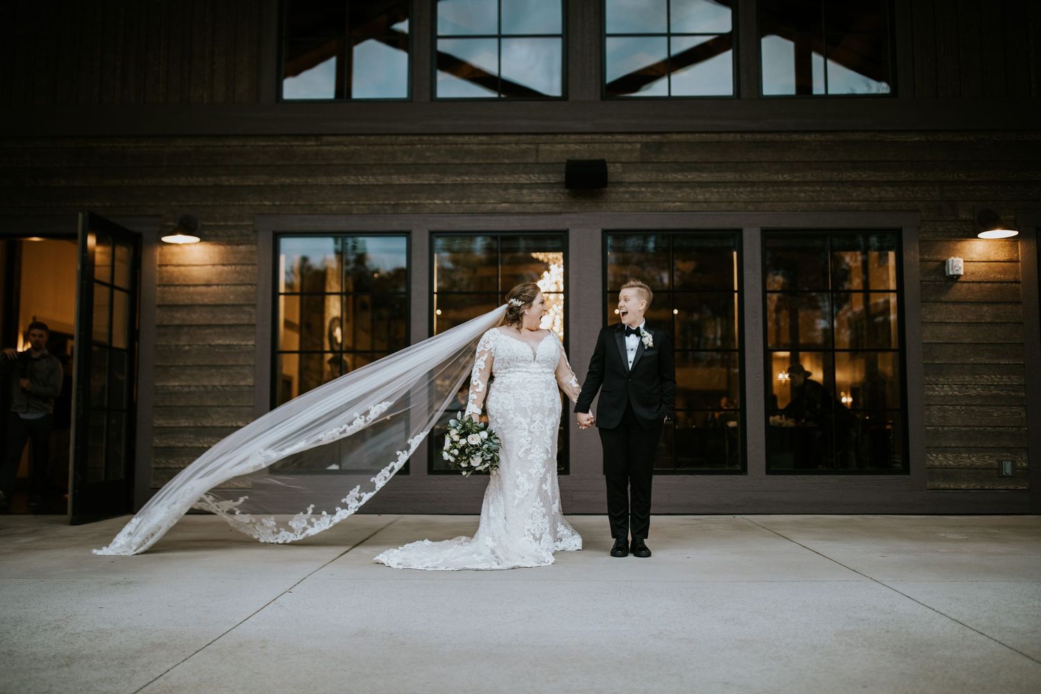 A bride and bride stand in a modern venue with dramatic lighting and wooden walls creating an elegant atmosphere.