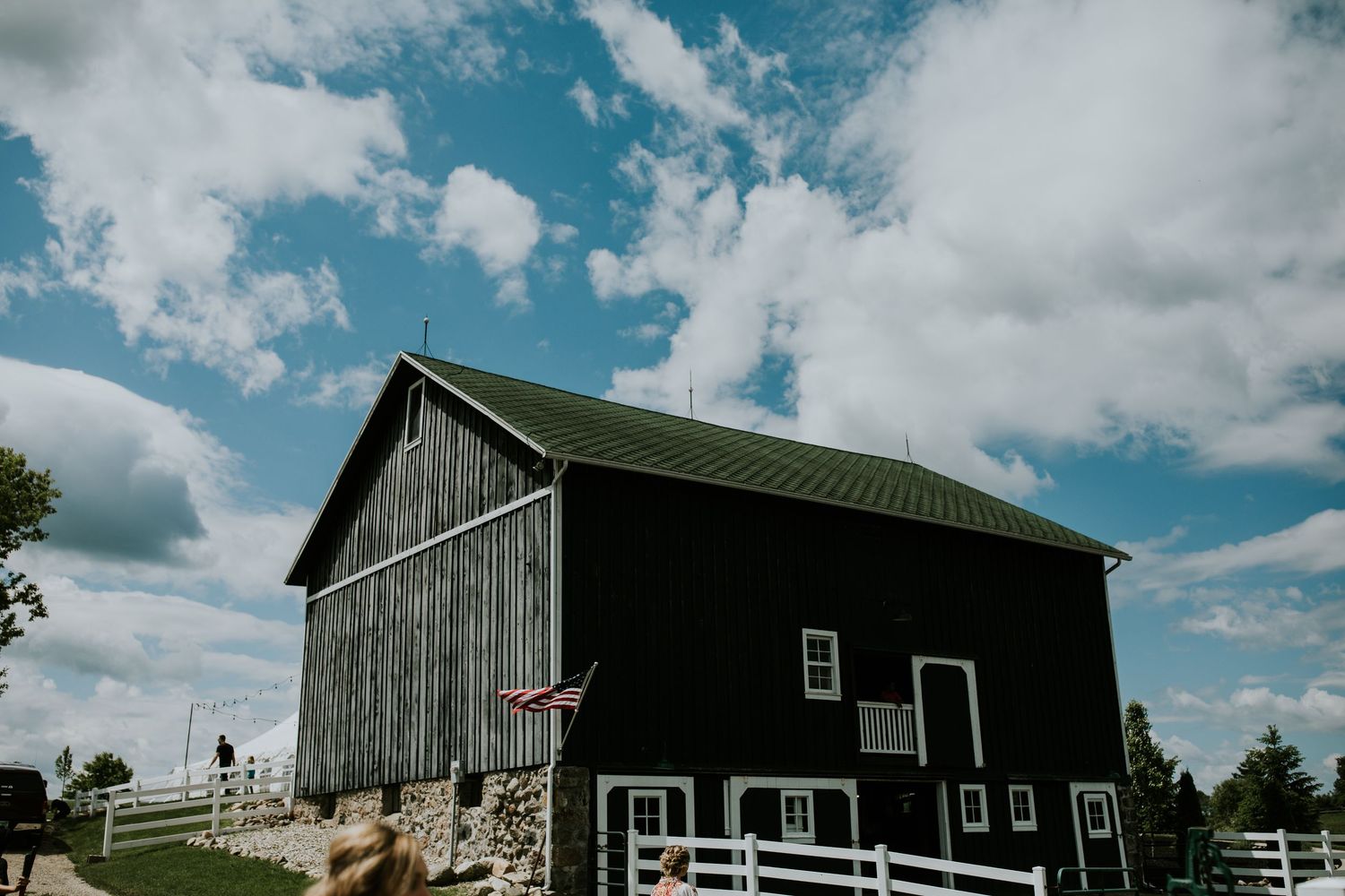 A panoramic view of rustic farm barns and buildings against a bright blue sky with white puffy clouds.
