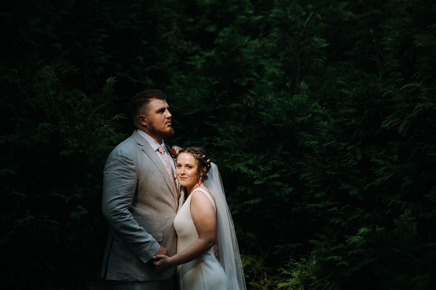 Dramatic wedding portrait of couple against dark forest backdrop.