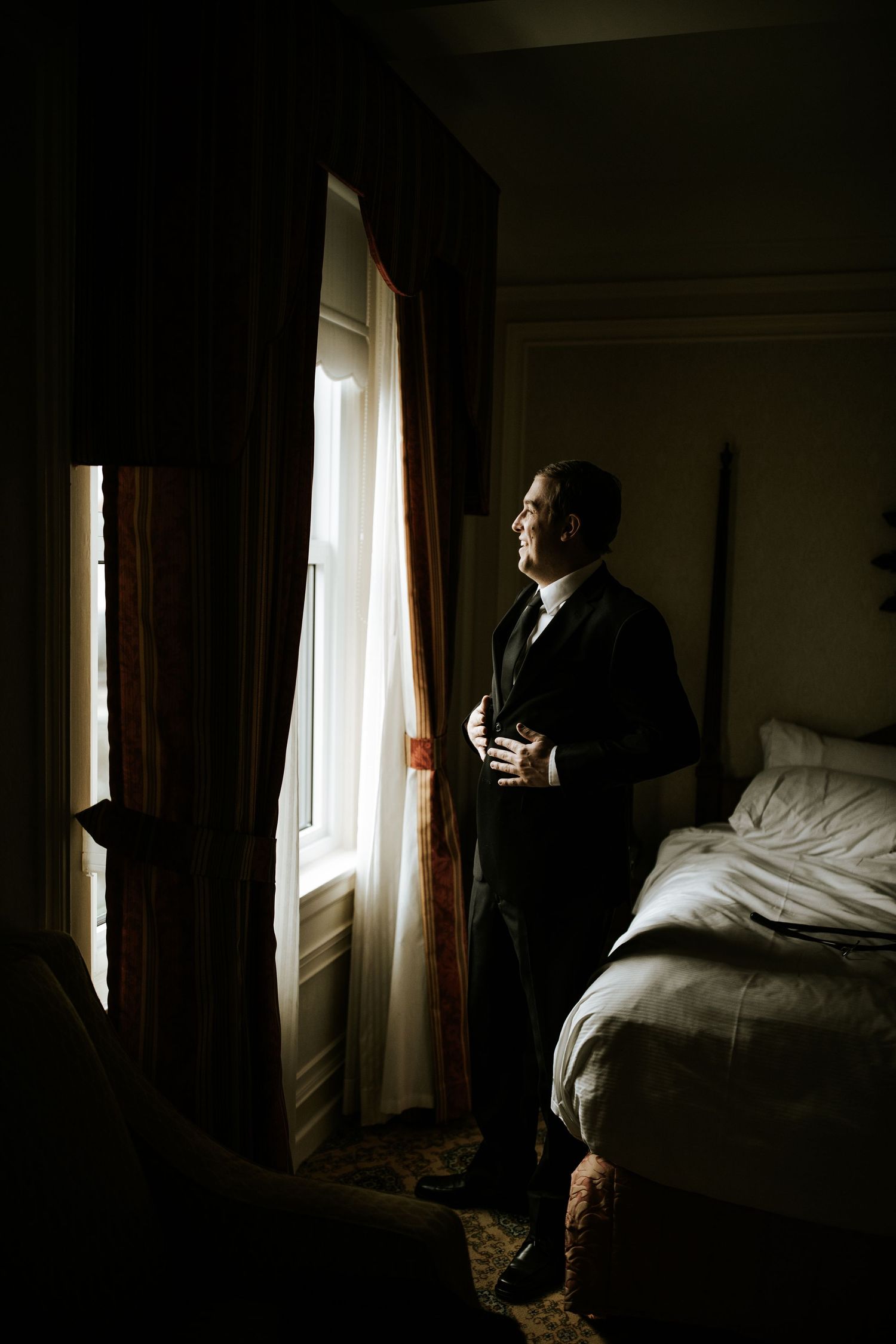 Silhouette of someone in formal attire gazing out a window in a dimly lit room.