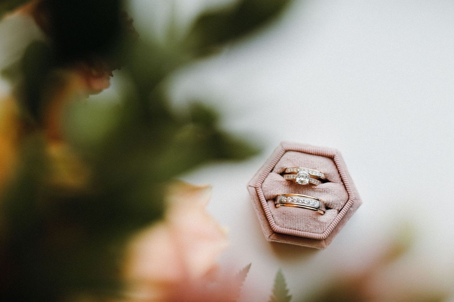 Wedding rings displayed in a pink hexagonal ring box with floral elements in background.