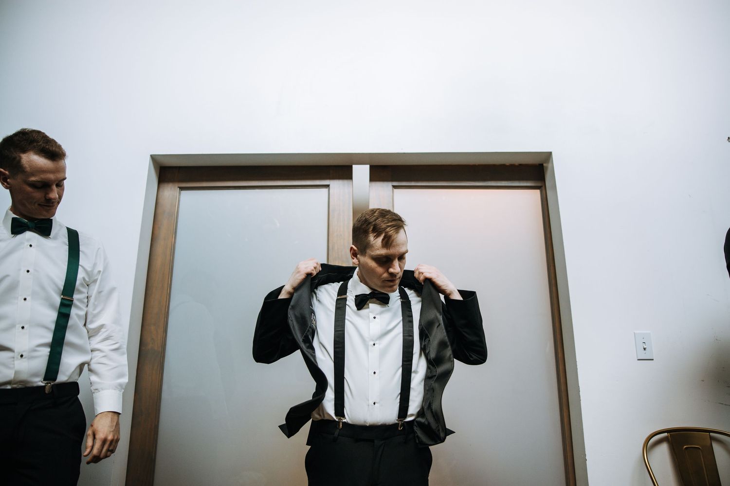 Groomsmen in formal attire adjusting bowties and suspenders before the wedding ceremony.