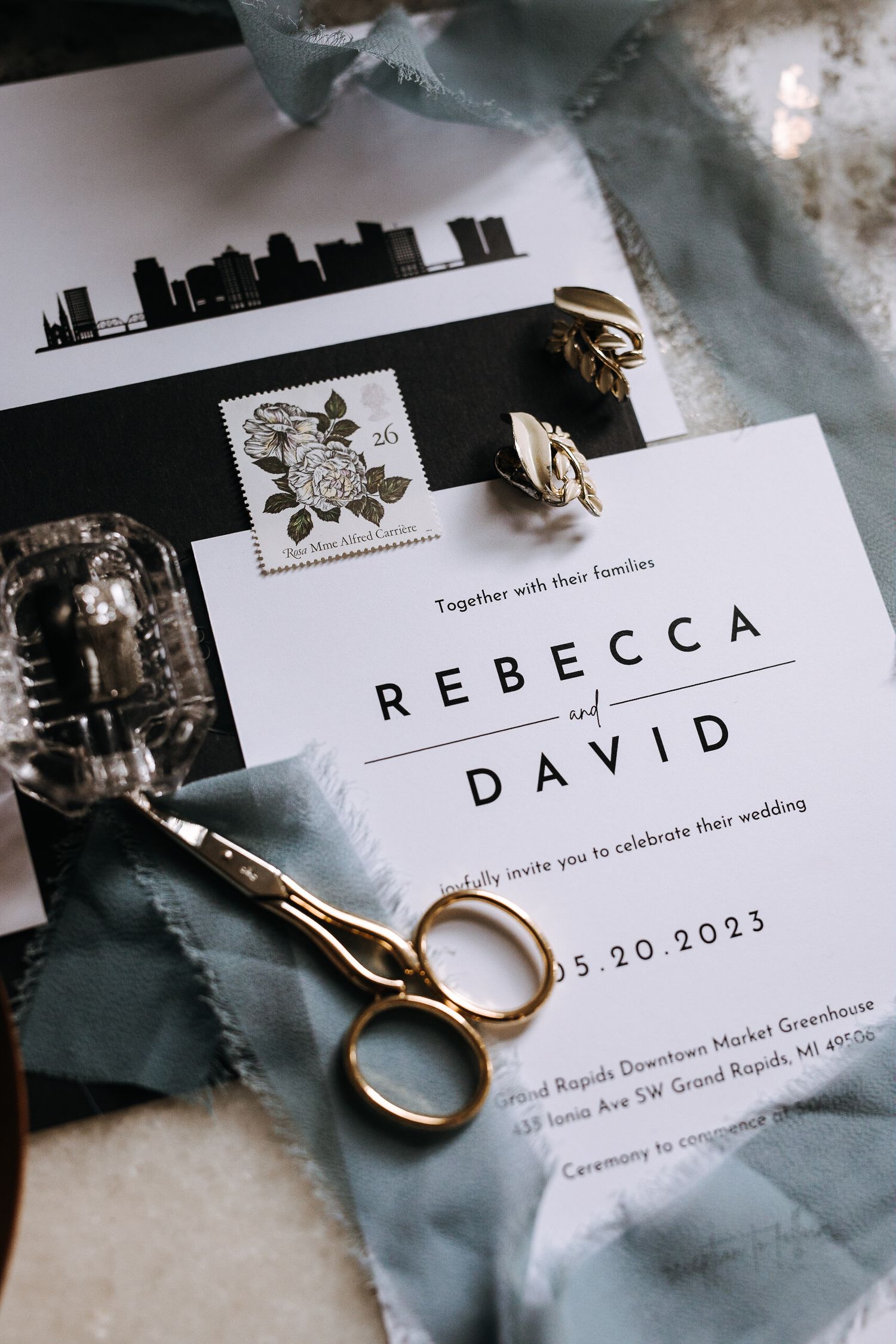Wedding invitation with city skyline design and gold rings on blue fabric.