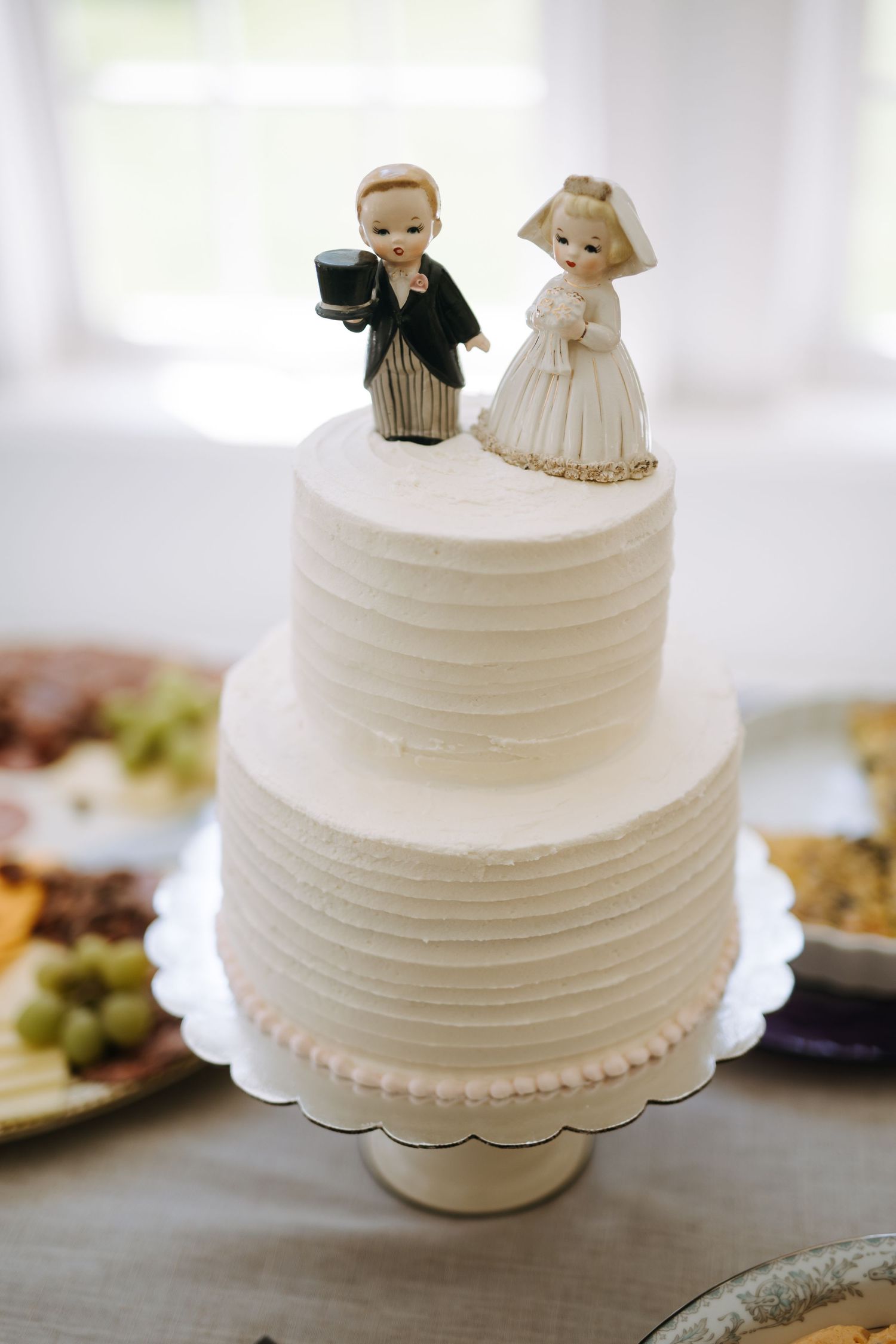 Simple white wedding cake decorated with bride and groom figurine toppers on display.