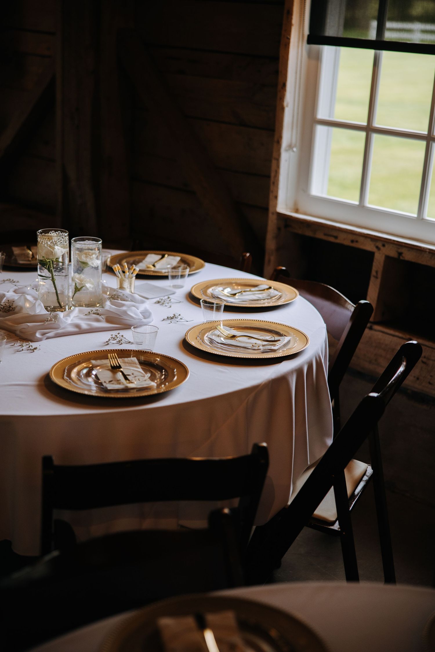 Elegant table settings with gold chargers and white linens in a rustic indoor venue.