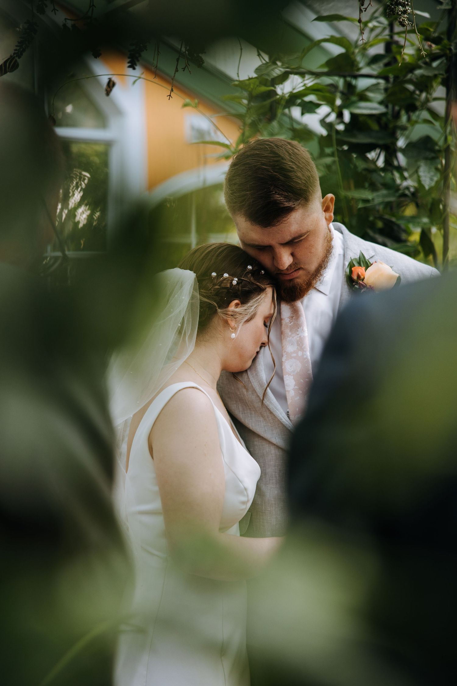 An intimate wedding moment captured through foliage in a garden setting.