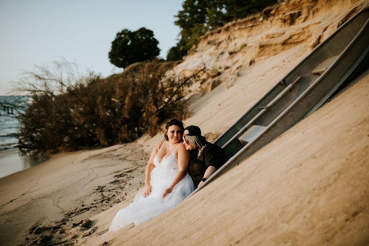 A couple in wedding attire walks along a sandy beach path during sunset.