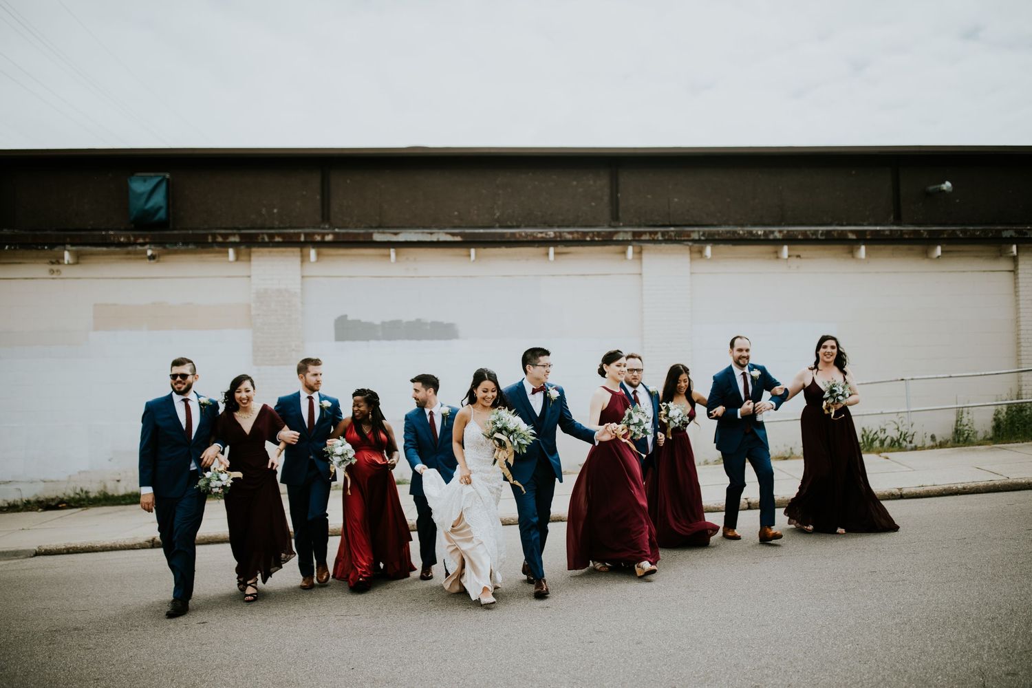 Wedding party stands in a line against a white wall creating a minimalist panoramic composition.