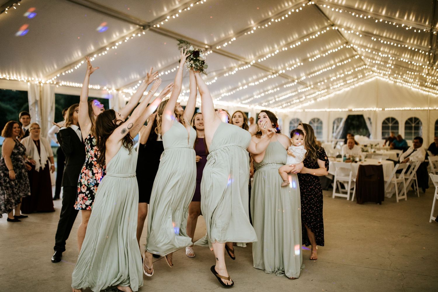 Guests enjoying a lively dance party under elegant string lights at an outdoor tent wedding reception.