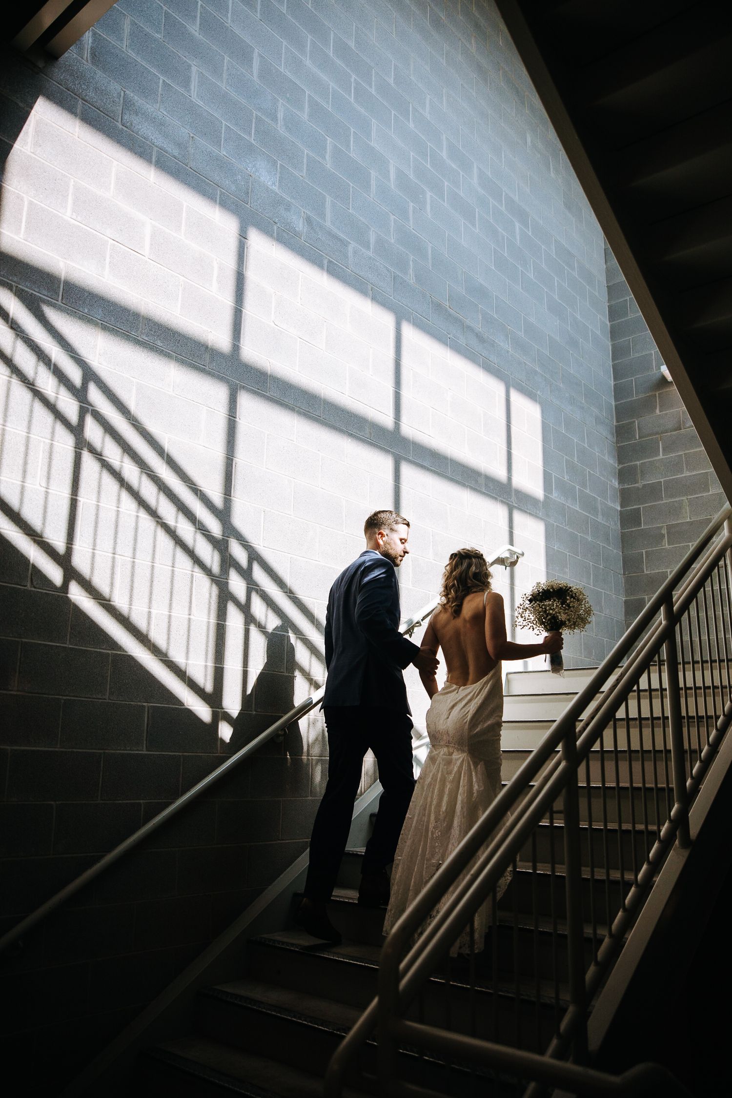 Dramatic stairwell wedding photos with shadows casting geometric patterns on wall.