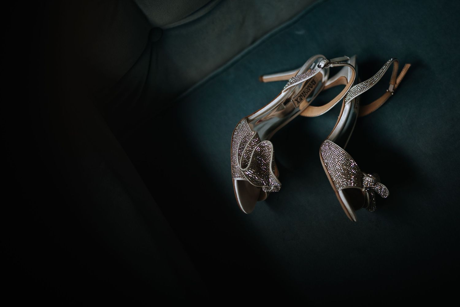 Sparkly silver wedding heels photographed on a dark teal background.