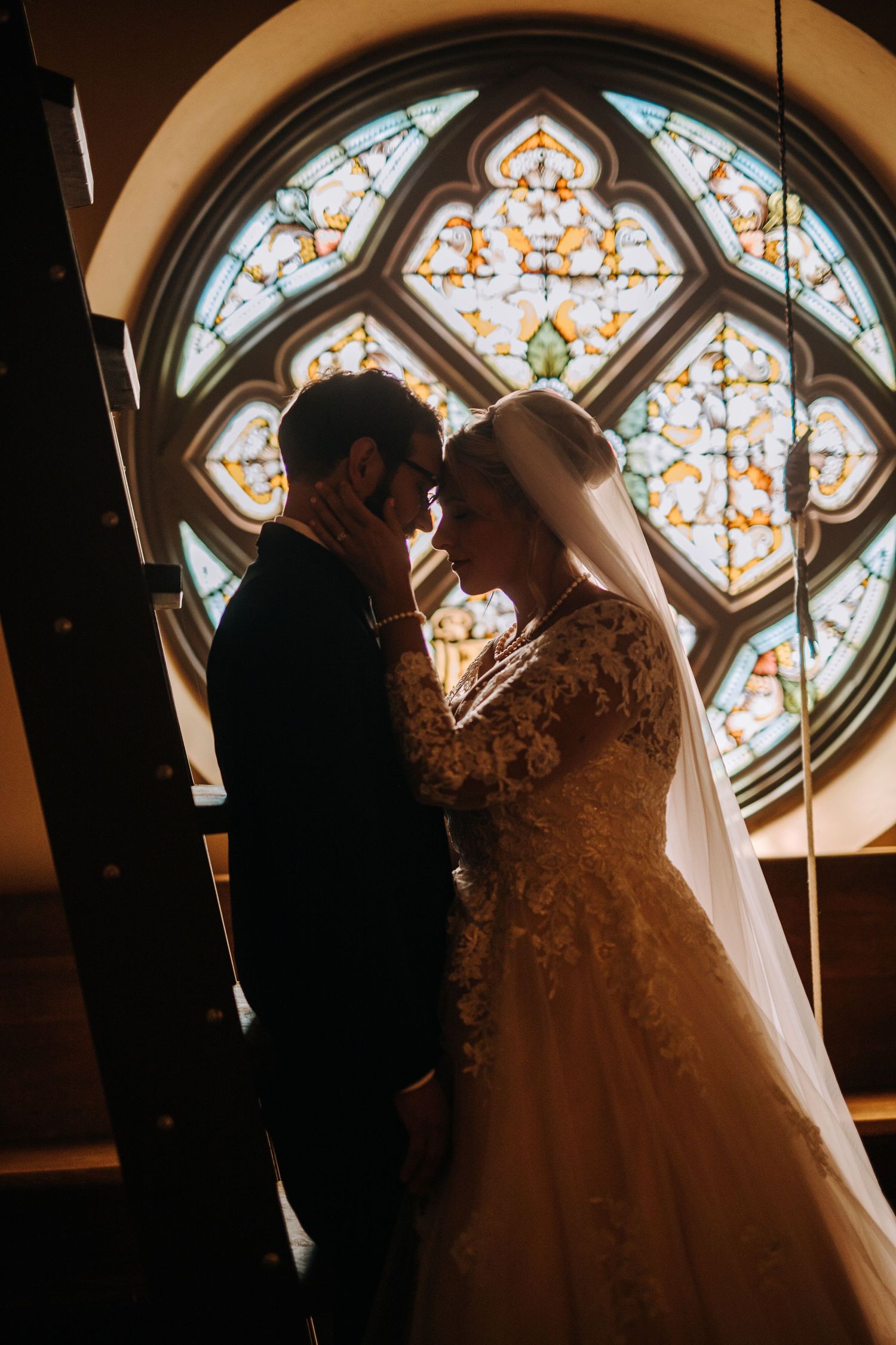 Silhouettes against ornate stained glass window create romantic wedding moment.