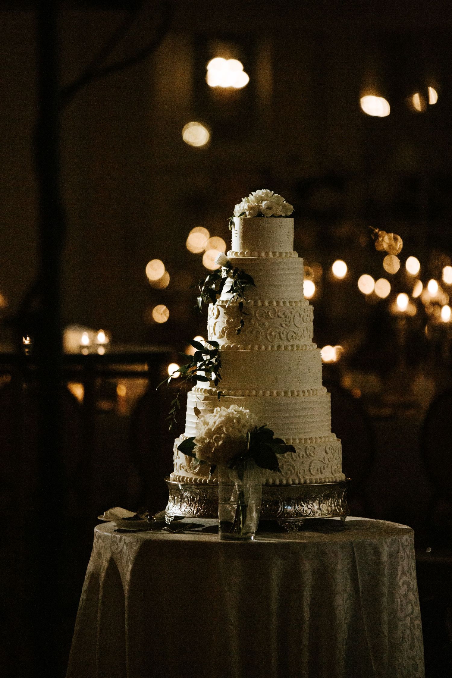 A white tiered wedding cake illuminated by soft lighting at an evening reception.