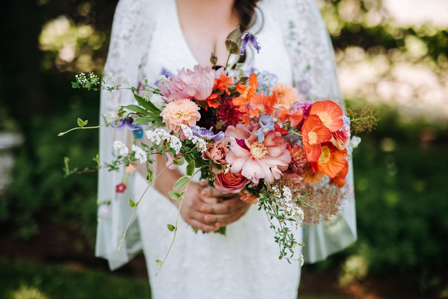 Close-up of hands holding vibrant coral and peach wedding bouquet against white lace.