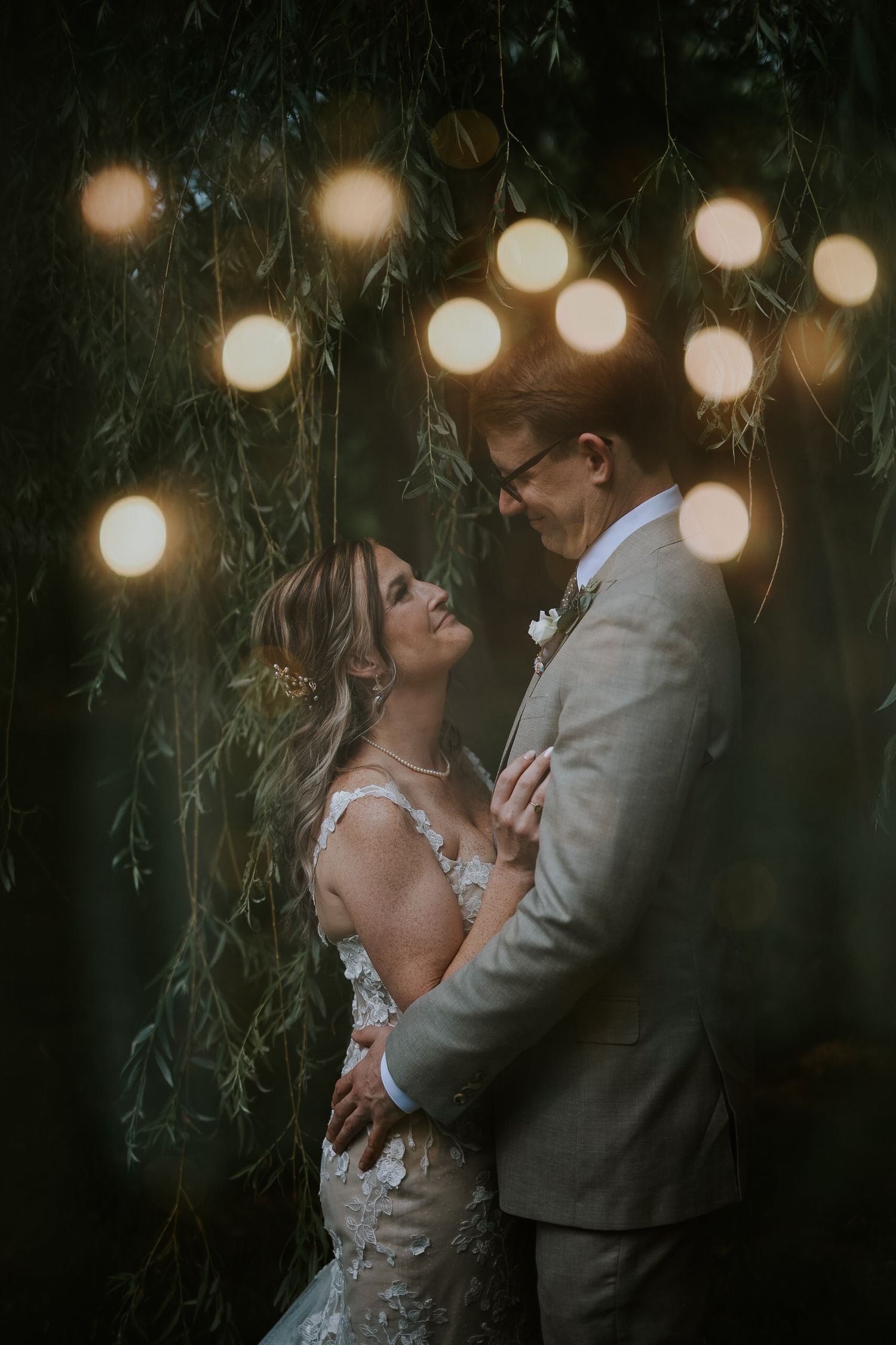 Romantic evening portrait with string lights and willow branches creating dreamy atmosphere.