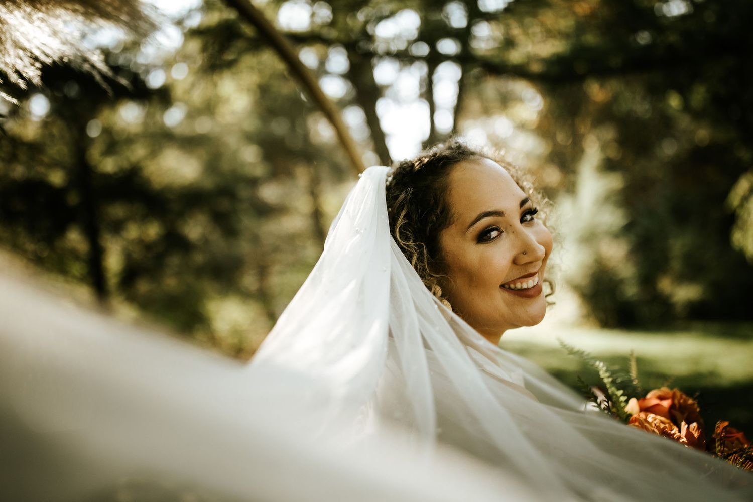 Wedding veil flowing in sunlit outdoor setting.