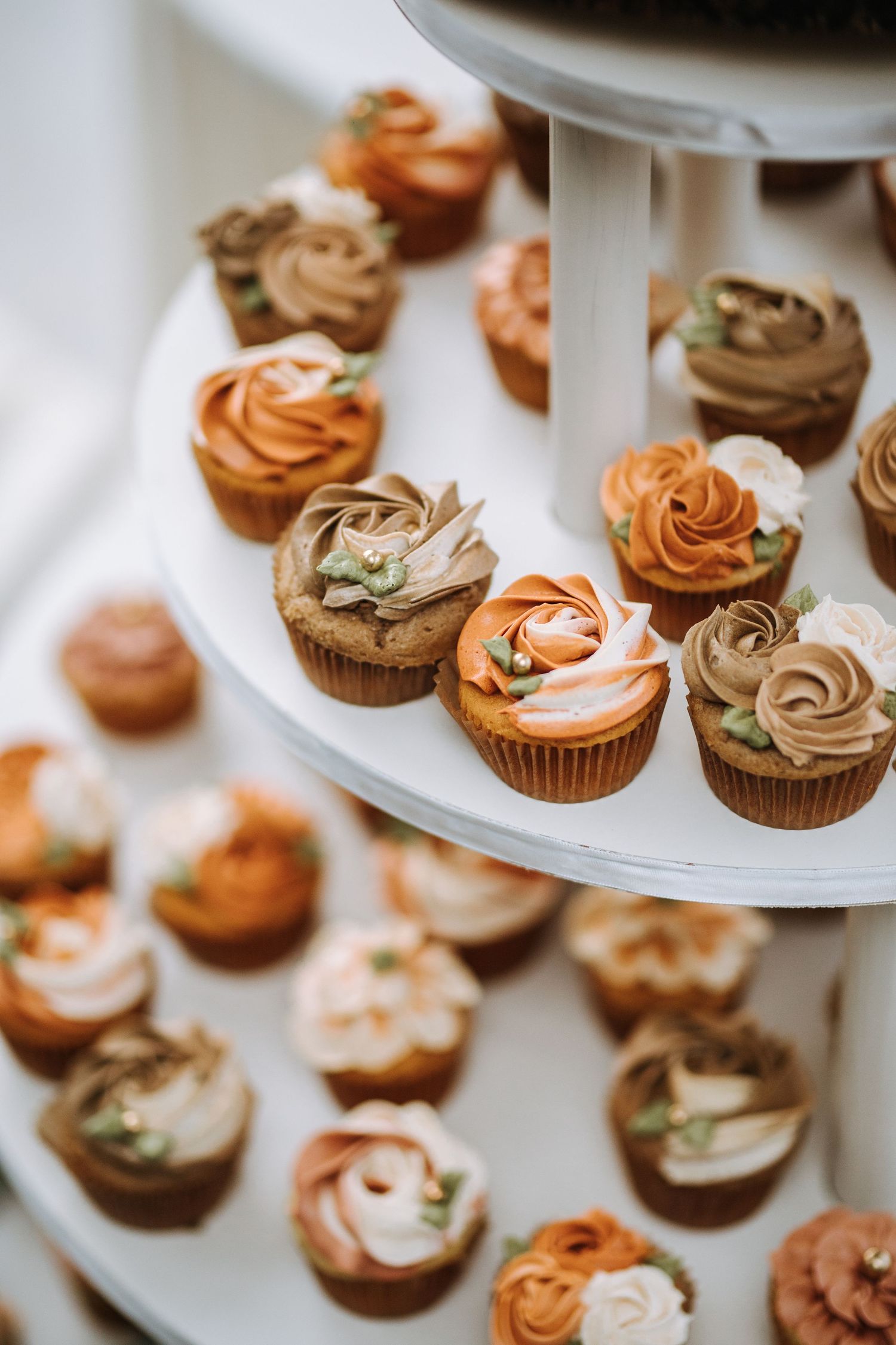Elegant cupcakes with swirled chocolate and peach-colored frosting arranged on a white tiered display stand.