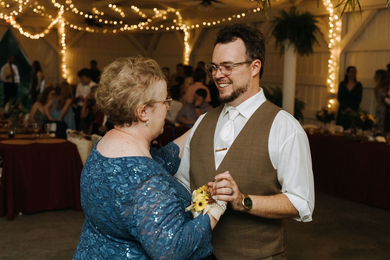 Pair dancing together under warm string lights at indoor reception.