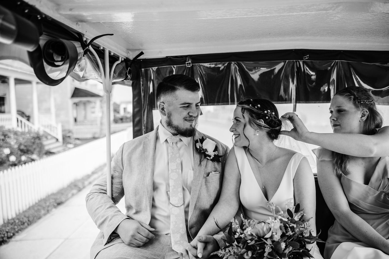Black and white photo of wedding couple riding in vintage car with decorative ribbons.
