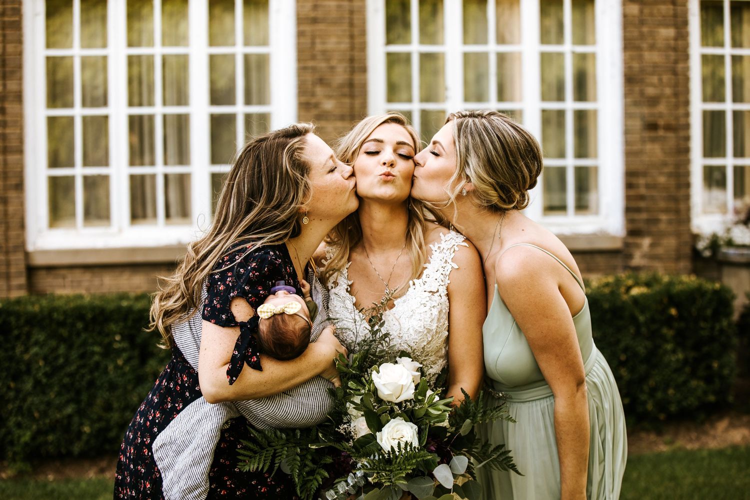 Wedding party sharing joyful moments in front of classic brick building with white windows.