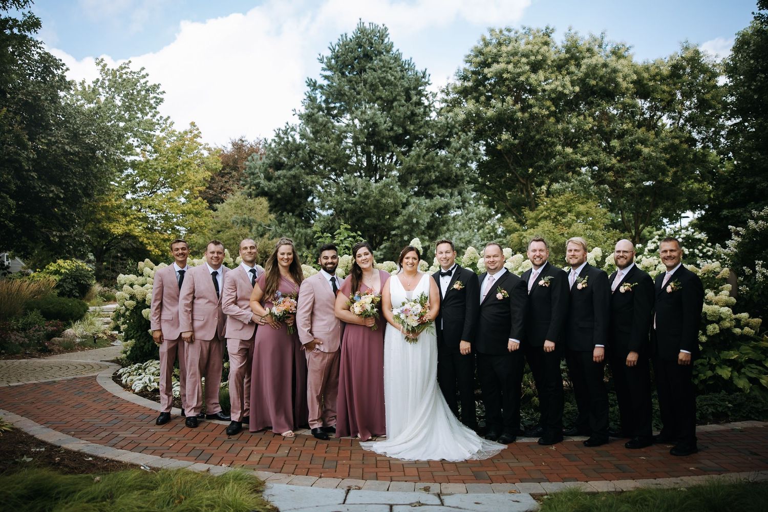 Wedding party in coordinated pink and black attire posed on a garden pathway.